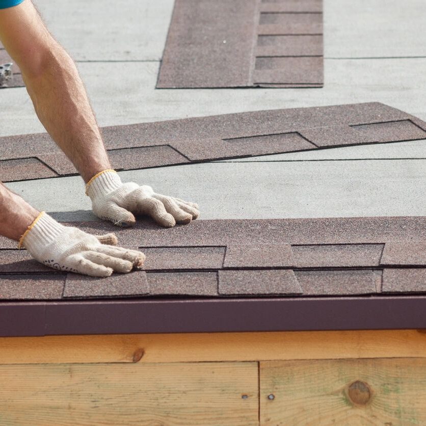 A person with gloves on working on the roof of a house.